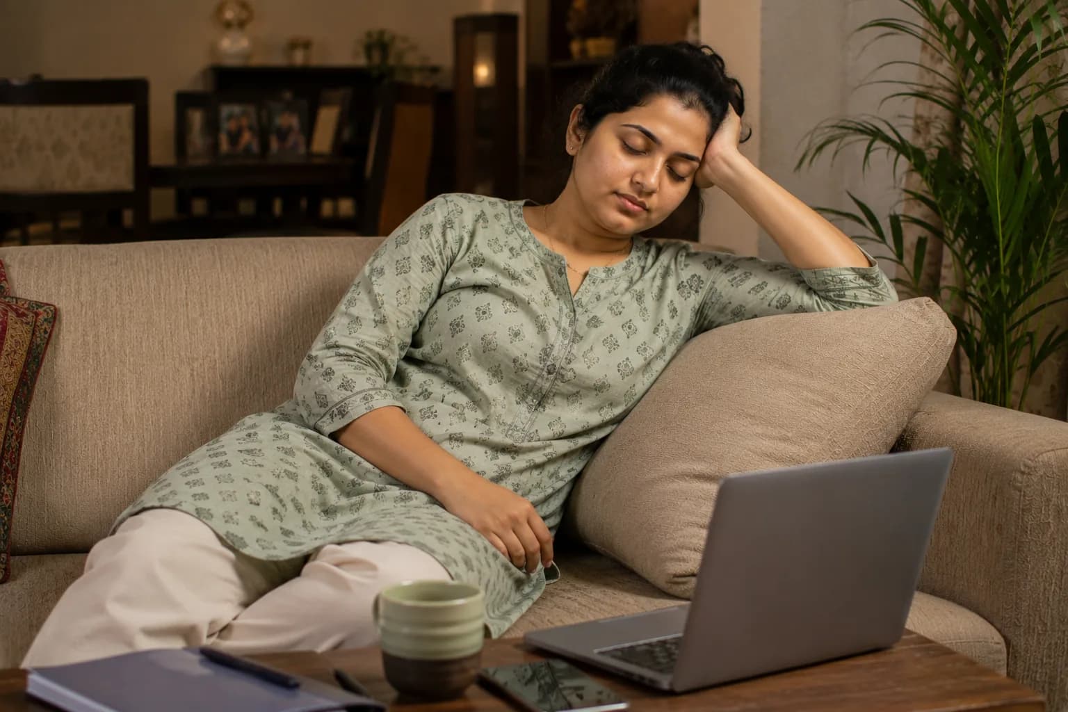 सोफ्यावर थकून बसलेली स्त्री, डोळे मिटलेले, समोर उघडा लॅपटॉप ठेवलेला